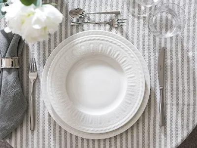 Elegante tafeldecoratie met wit Cellini bord met reliëf, bestek en gevouwen grijs servet.