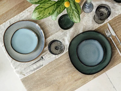 Lave Collection Plates – Top View of a Modern Table Arrangement Top-down view of a modern table arrangement featuring dinner and bread plates from Villeroy & Boch’s Lave collections: Lave Vert, Lave Beige, and Lave Glacé. The clean composition highlights the unique reactive glazes and natural textures of each plate on a neutral tabletop, with no food present, emphasizing the artisanal elegance of the stoneware