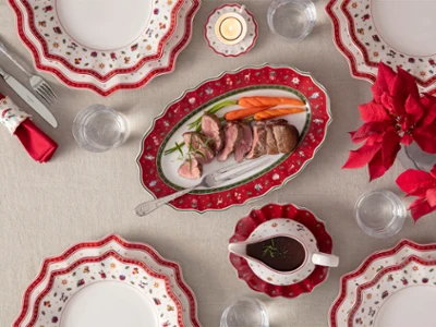 Toy's Delight serving platter & meat fork Top-down view of Toy's Delight plates, red oval platter with sliced meat, a stainless steel meat fork, and a gravy boat on a festive table.