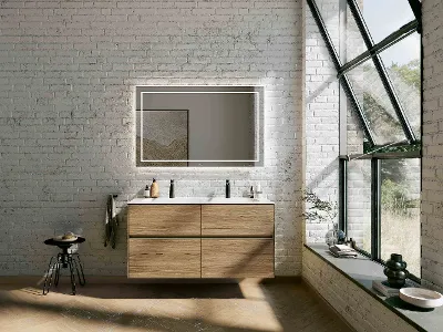 Lavabo doppio Finion marrone con specchio illuminato Bagno moderno con mobile lavabo sospeso in legno Finion, grande specchio illuminato, pareti in mattoni e ampie finestre. Ha uno sgabello nero e decorazioni sulla mensola e lungo il davanzale.