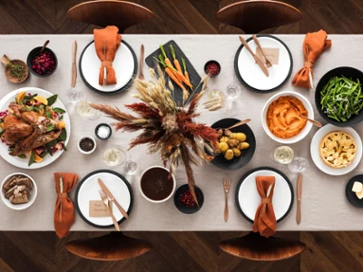 NewMoon and Manufacture Harvest Thanksgiving table A table set with dishes, roast turkey, vegetables, mashed potatoes, greens, bread, and an autumnal floral arrangement in the center.