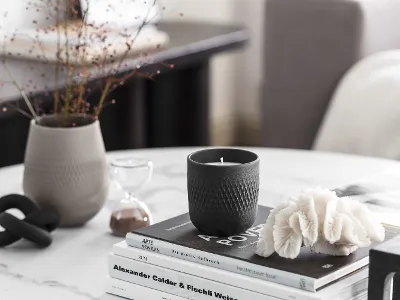 Manufacture scented candle and vase on marble table Elegant home decor arrangement with a black Manufacture scented candle, books and a light gray Manufacture vase on a marble table.