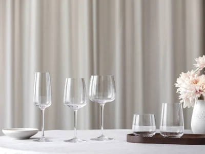 Afina glasses without drinks Elegant table setting with four crystal glasses and a white vase of pink flowers on a white tablecloth against a soft, neutral background.