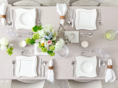 White elegance with NewWave Elegant table setting with white square plates, napkin rings, neatly arranged cutlery, a floral centerpiece with white and green flowers, and a glass pitcher with lemon slices.