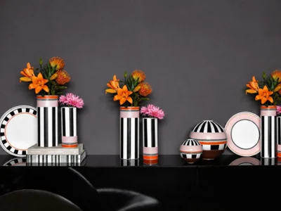 Memphis vases on shelf with la boule and plates Black and white striped vases hold orange and pink flowers, arranged with matching striped plates and bowls on a glossy black surface against a dark gray background.