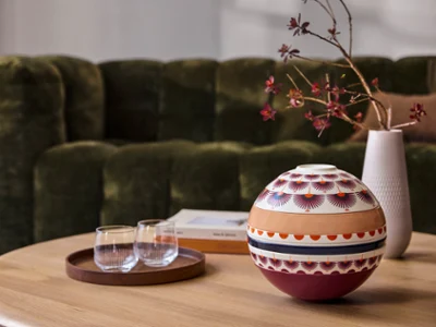 Una mesa La Boule Kyoto y una bandeja con vasos sobre una mesa de centro de madera, frente a un sofá verde.