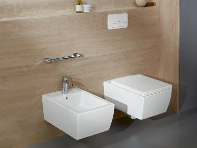 WC e bidet bianchi della collezione Memento 2.0 Bagno moderno con WC e bidet bianchi a parete davanti a muri con piastrelle beige, dotato di rubinetteria cromata, sciacquone ed elegante portasciugamani.