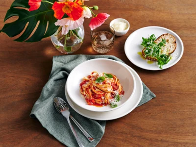 Artesano Original Dinner Set for Four Artesano dinner set for four, arranged on a rustic wooden table, features a delicious spread of pasta and fresh bread. Accented with a blue linen napkin and silver cutlery, the setting is further elevated with elegant Like glassware and a vase filled with florals.