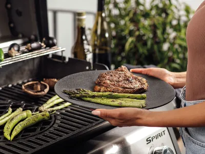 Set de barbecue élégant avec assiette noire Manufacture et femme au grill Une table élégamment dressée avec une assiette noire Manufacture faisant partie d’un set de barbecue, tandis qu’une femme est au grill – une touche moderne pour les barbecues.