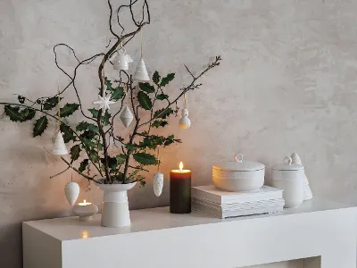 Modern, minimalist Christmas decoration on a white shelf with Winter Glow vase, branches, and hanging ornaments. 