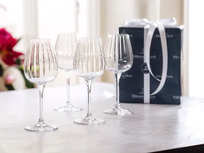 Four crystal wine glasses on a table next to a wrapped gift box with a white ribbon. Four crystal wine glasses on a table next to a wrapped gift box with a white ribbon.