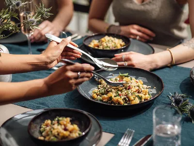 Lave bowls with mixed salad are placed on a blue tablecloth. Four people enjoy a meal at one table. Lave bowls with mixed salad are placed on a blue tablecloth.