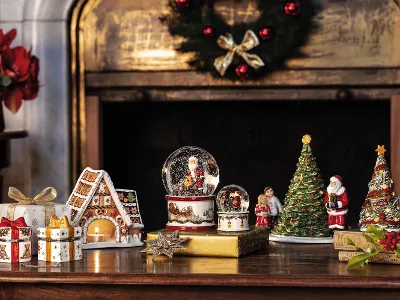 Christmas toys decorative figures in front of a cozy fireplace A cozy fireplace scene with a wreath, Santa Claus snow globes, a Christmas tree figure, a gingerbread house, presents, and the toy car “A Christmas Toy” from Villeroy & Boch on a wooden mantelpiece.