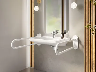 Lavabo ViCare con maniglioni bianchi Un lavabo ViCare con maniglie pieghevoli e uno specchio con illuminazione d'ambiente su una parete intonacata di grigio.