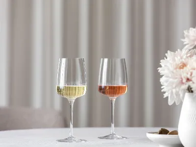Two Villeroy & Boch Afina wine glasses are placed on a table next to a vase with pink flowers. Two Villeroy & Boch Afina wine glasses, one filled with white wine and the other with rosé, are placed on a table next to a vase with pink flowers.