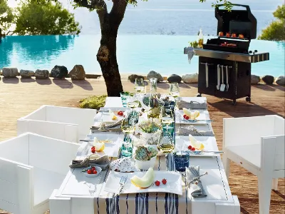 New Wave outdoor dining table by the pool with food, barbecue and view of the water.
