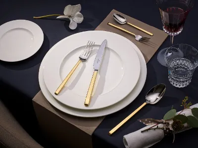 La Classica dinnerware with gold accents on white plates Create an elegant table setting with the La Classica collection from Villeroy & Boch, complete with white plate, gold flatware, wine glass, water glass, napkin, and a decorative orchid on a dark tablecloth.