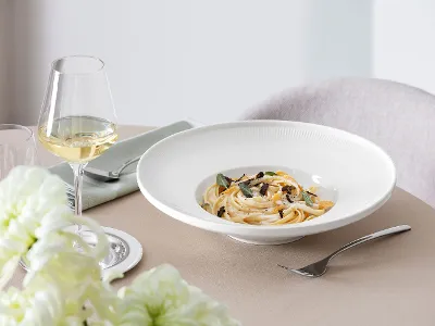 Afina pasta plate with pasta, mushrooms and herbs An Afina plate with pasta, mushrooms and herbs, accompanied by a glass of white wine on an elegantly laid table.