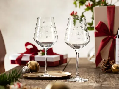 A pair of Villeroy & Boch Toy's Delight wine glasses on a table surrounded by wrapped gifts, a bottle of wine and festive decorations.