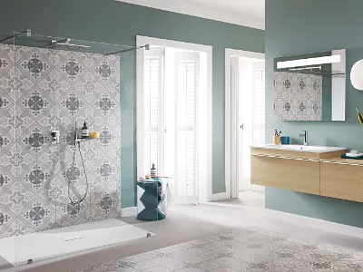 Bagno con doccia in vetro Venticello e mobile lavabo in legno Bagno moderno con doccia in vetro, rivestimenti con motivi artistici, lavabo sospeso in legno, grande specchio e lampade bianche a sospensione. La stanza ha pareti verde tenue e la luce naturale entra attraverso due finestre.