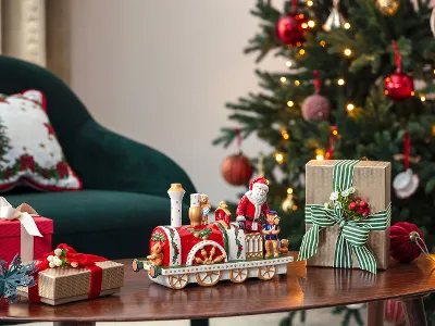 Un albero di Natale decorato, regali e una locomotiva Christmas Toys Memory su un tavolo di legno accanto a una sedia verde.