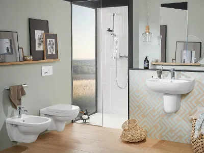 Bagno moderno con WC, bidet, lavabo e doccia della collezione O.novo Il bagno moderno con piastrelle beige e pareti color pastello è dotato di un WC a parete O.novo, un bidet, un lavabo con specchio e una doccia a filo pavimento. Le mensole hanno quadri incorniciati e articoli da toilette. Ci sono cesti sul pavimento.