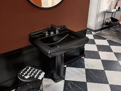 Un lavabo Hommage nero con rubinetto moderno davanti a una parete rossa, un pavimento a scacchi bianchi e neri e un tavolino rotondo con un asciugamano piegato.
