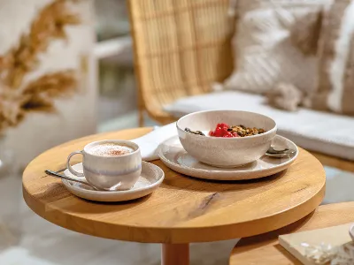 Perlemor cup with coffee beside a bowl A Perlemor cup with coffee and a bowl of muesli on a wooden table.