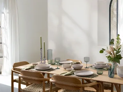 Modern dining table setting with Villeroy & Boch like ice glassware, perlemor sand porcelain, wooden chairs and natural decoration in bright room with open windows