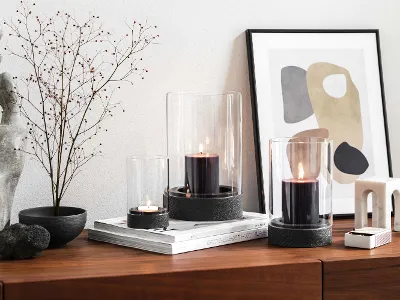 A modern home interior with a wooden sideboard and dried flower with three Manufacture hurricane lamps.