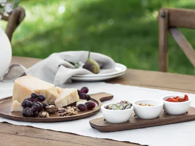 The wooden board from the Artesano collection by Villeroy & Boch presents cheese, grapes and walnuts The wooden board from the Artesano collection by Villeroy & Boch presents cheese, grapes and walnuts accompanied by three small bowls with different toppings. A vase and stacked plates add to the aesthetics of the background.