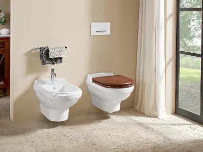 WC Hommage con coperchio in legno e bidet bianco Un bagno ha un bidet sospeso e un WC con coperchio in legno, pareti beige, pavimento piastrellato e finestra con tende bianche.