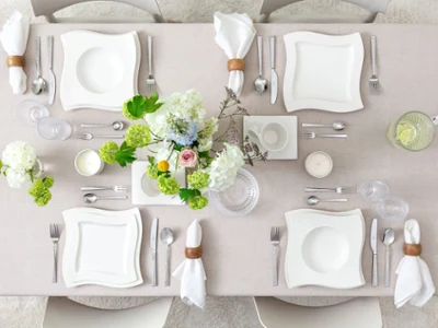 Minimalist Table Setting with NewWave & Boston Green Vue du dessus d’une table minimaliste avec assiettes en porcelaine NewWave, tasse à café et soucoupe, verrerie Boston et Boston Green, et couverts NewWave et Blacksmith. Des vases de fleurs ajoutent une touche naturelle et élégante à la composition épurée.