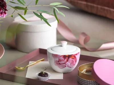 Rose Garden sugar bowl with a gold spoon on a tray A Rose Garden sugar bowl with a candle, a gold spoon, a chocolate truffle and decorative items on a tray.