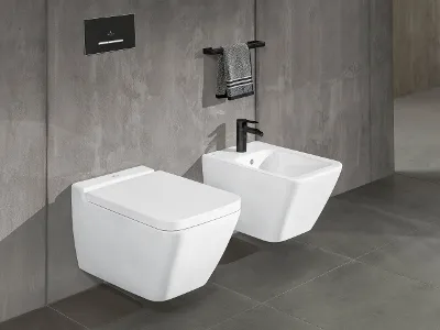 Hvidt toilet og bidet fra Finion-kollektionen Et moderne badeværelse med et hvidt væghængt Finion-toilet og et hvidt bidet. Der er en sort skylleplade over toilettet og en sort håndklædestang med et gråt håndklæde på en grå flisevæg over bidetet.