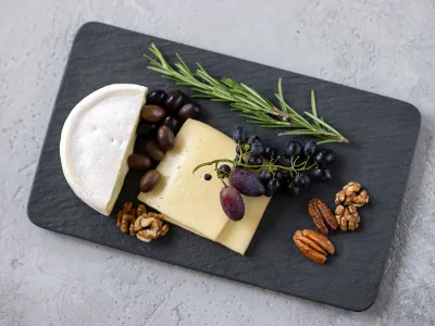 Black Manufacture serving platter as a cheese platter Manufacture square black serving platter with slices of cheese, a piece of soft cheese, olives, grapes, walnuts, pecan nuts and a sprig of rosemary.