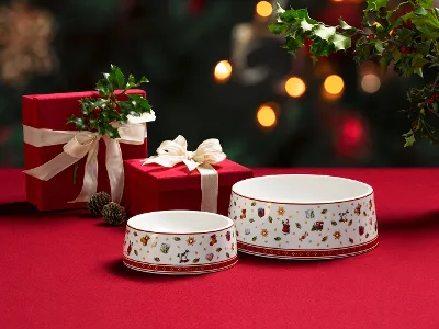 Zwei Toy's Delight Näpfe für Haustiere mit weihnachtlichen Motiven Zwei Toy's Delight Näpfe für Haustiere mit weihnachtlichen Motiven auf einem roten Tuch, daneben zwei rote Geschenkboxen mit weißen Bändern und Grünzeug.