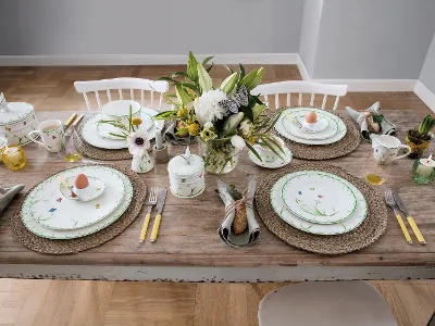 Subtly set Easter table with Colorful Spring dinnerware A “Colourful Spring” dinner set for four from Villeroy & Boch consists of porcelain with a floral pattern, flatware with yellow handles, woven placemats, and a floral arrangement. Each place setting includes an egg in a decorative cup.