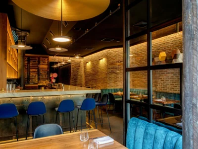 Arvine NYC restaurant and bar Warm, stylish restaurant interior with exposed brick walls, pendant lights, blue bar stools, and teal seating around a glowing bar.
