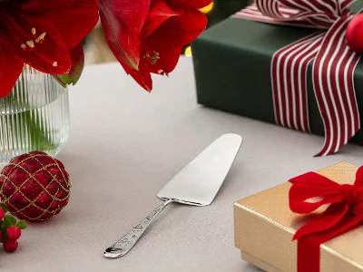 A cake server on a table with red flowers, wrapped gifts, and Christmas decorations.