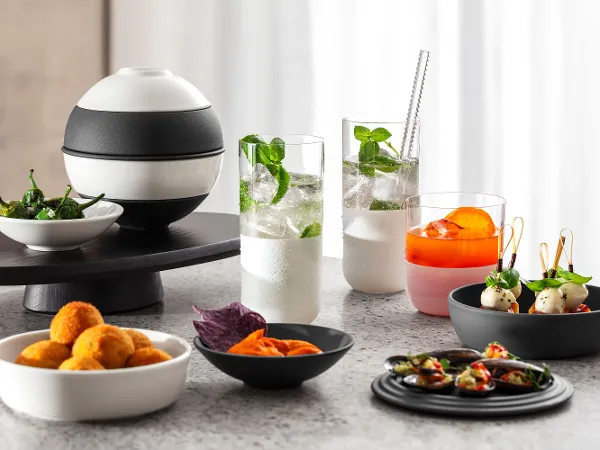 La petite Boule black and white presented on a marble worktop La petite Boule black and white presents various appetizers on a marble countertop, including deep-fried canapés, purple chips, skewers, and drinks with garnishes.