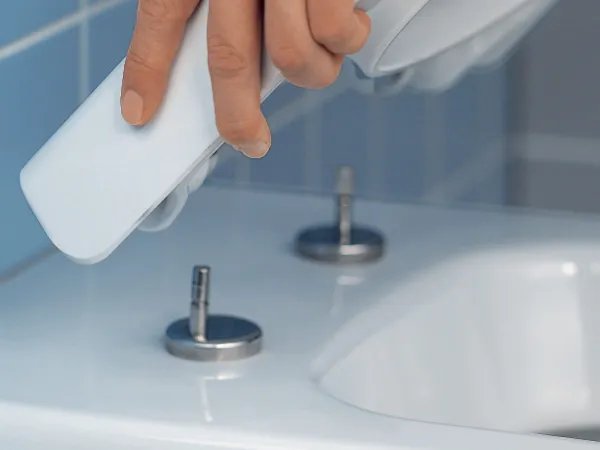 Subway 2.0 WC-Sitz wird von Toilette abgenommen Eine Hand entfernt einen Toilettensitzbezug in einem Badezimmer mit blau gefliesten Wänden.