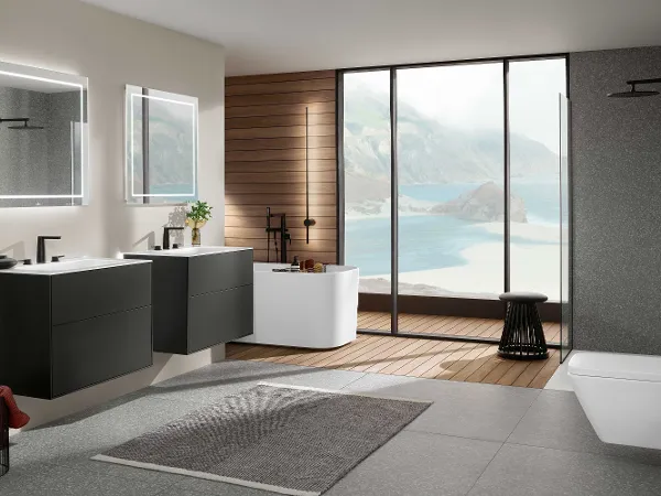 Cuarto de baño Finion con dos lavabos, bañera exenta y ducha acristalada Moderno cuarto de baño con lavabos dobles flotantes Finion, espejos iluminados, bañera exenta, ducha acristalada y grandes ventanales con vistas al mar. Mobiliario minimalista con una mezcla de superficies de madera y piedra.