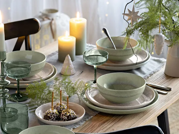Festliche Tafel mit Perlemor Tellern und Winter Glow Dekorationen Festliche Tafel mit grünem und beigem Perlemor Tellern, umgeben von Winter Glow Kerzenhaltern und Like Gläsern.