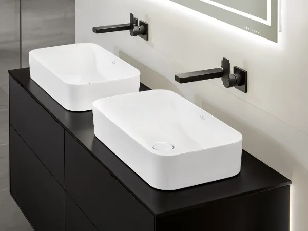 Zwei weiße Finion-Waschbecken mit schwarzen Wandarmaturen Ein moderner Badezimmerwaschtisch verfügt über zwei rechteckige weiße Aufsatzwaschbecken mit dazu passenden schwarzen Wandarmaturen. Der Waschtisch hat eine mattschwarze Oberfläche und darüber einen rechteckigen Spiegel.