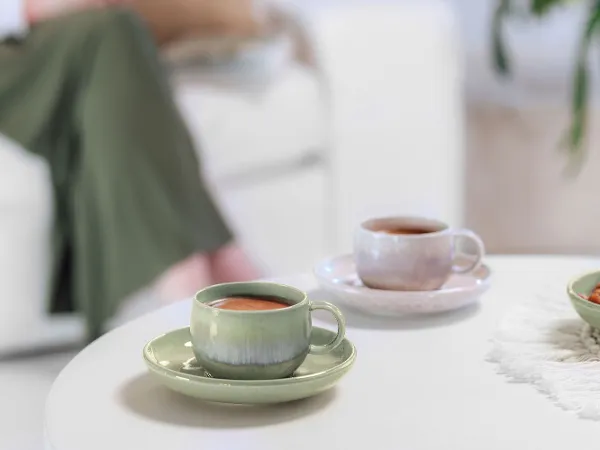 Kaffeezeit mit Perlemor im gemütlichen Wohnzimmer Zwei Perlemor Kaffeetassen auf einem Wohnzimmertisch, im Hintergrund eine teilweise sichtbare Person auf dem Sofa.