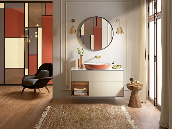Oranje Artis wastafel op Finion onderkast Moderne badkamer met oranje Artis wastafel, ronde spiegel, beige Finion badmeubel en minimalistische decoratie