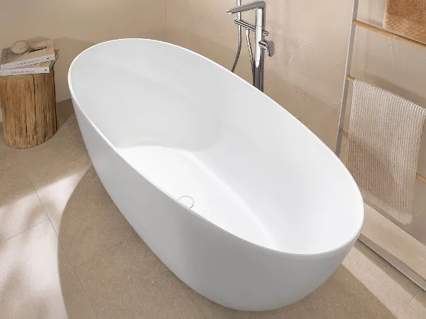 Formschöne Antao Badewanne mit Armatur Eine weiße freistehende Badewanne in einem beigen Badezimmer mit Fenster