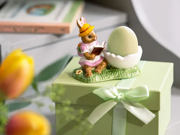Annual Easter Edition 2025 – Lapin lisant avec œuf L'« Annual Easter Edition 2025 » de Villeroy & Boch présente un lapin lisant à côté d’un œuf sur une boîte cadeau emballée.