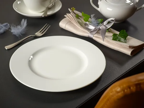 Ein weißer Anmut Teller auf einem Tisch Ein weißer Anmut Teller auf einem Tisch mit einer Gabel, einer gerollten Serviette, dekorativen Federn, einer Teekanne und einer Tasse mit Untertasse.